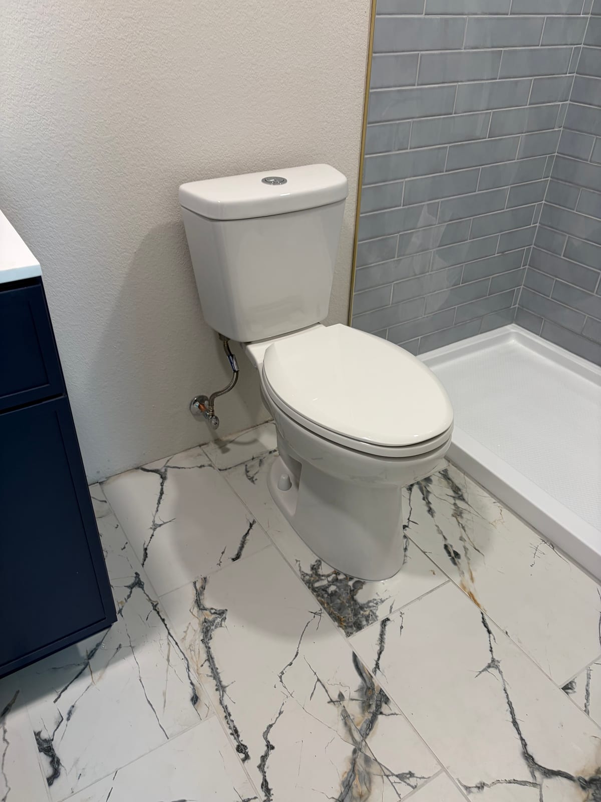 White dual-flush toilet beside a tiled shower and navy vanity