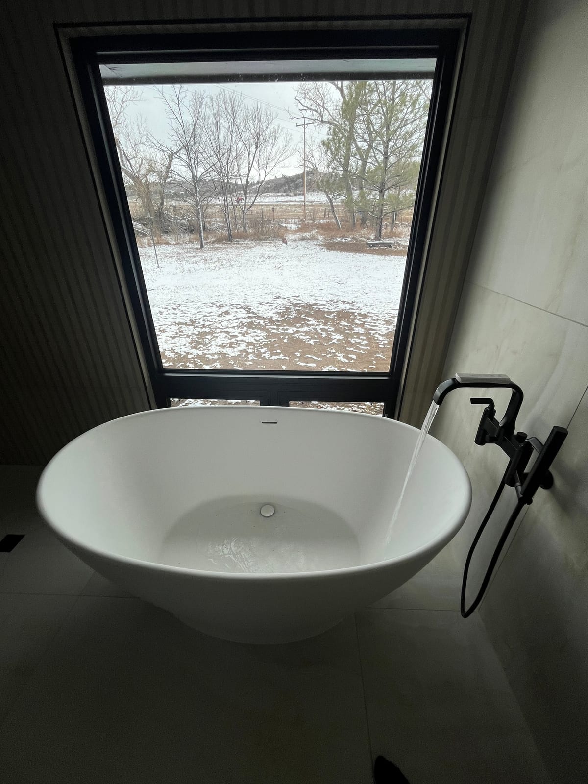 Freestanding bathtub with water flowing from a matte-black floor-mounted faucet
