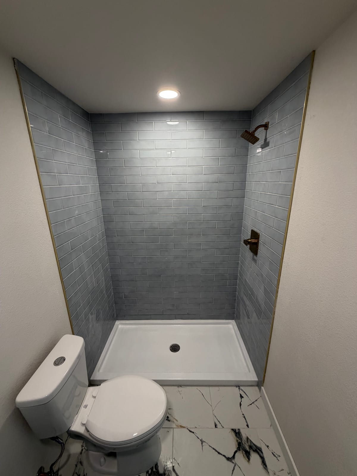 Gray subway-tile shower with brass fixtures and a white shower base