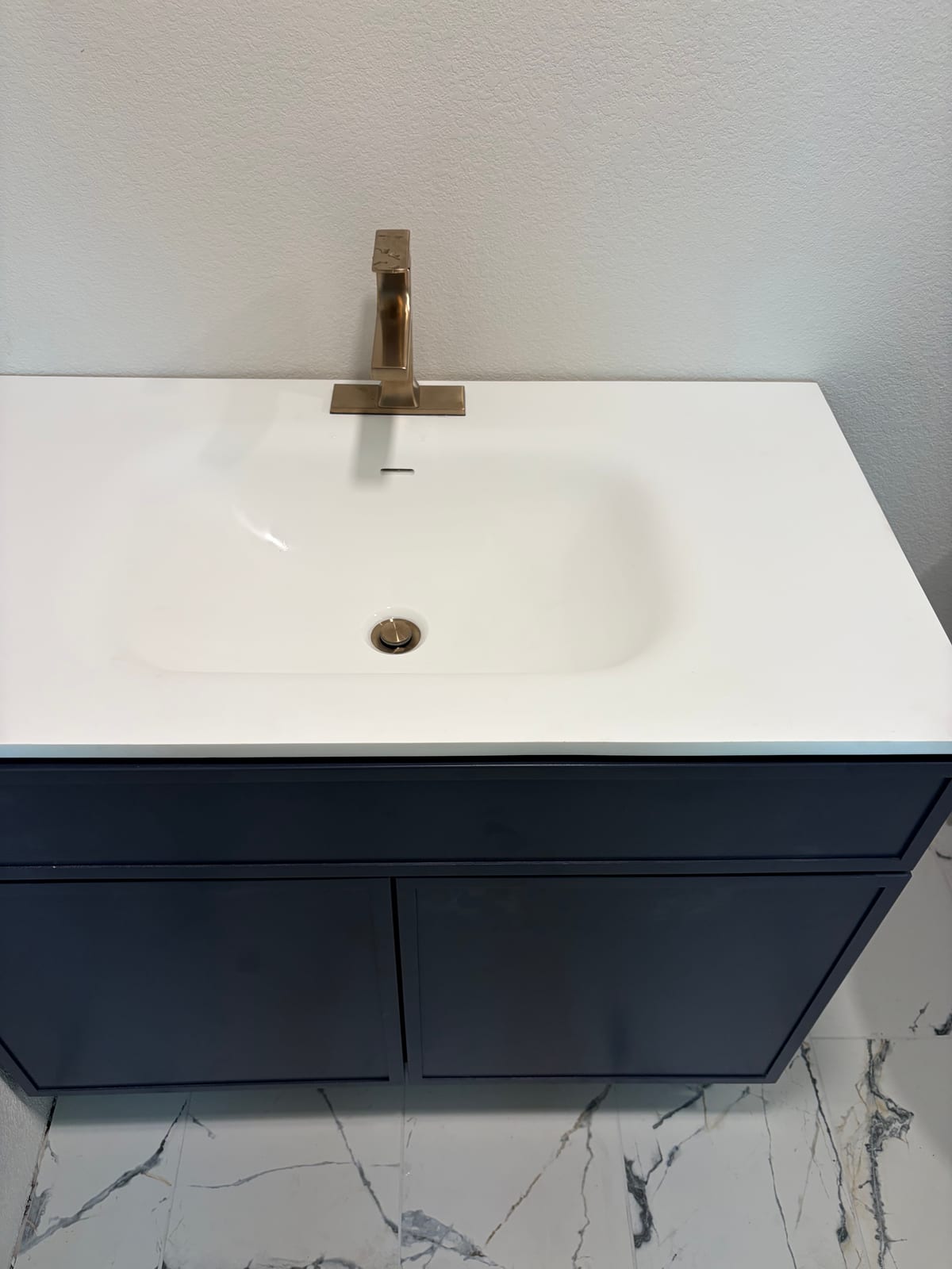 White bathroom sink with a brass faucet and navy vanity cabinet